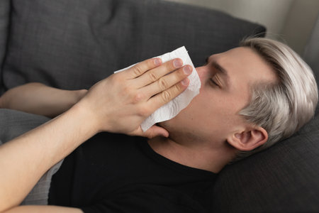 A man with white hair is sick and blows his nose into a paper napkin