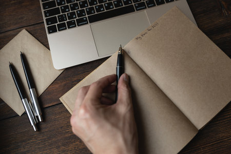 A man writes in a notebook My plans for 2021 with a pen on a dark wooden table.の写真素材