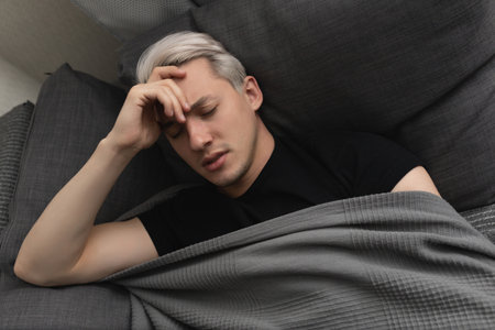 Man with white hair is sick while lying on the sofa at home