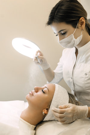 doctor cosmetologist applies a spray to the patients faceの写真素材