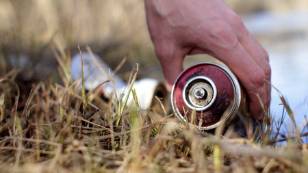 Hand of volunteer picking up litter can from river shore