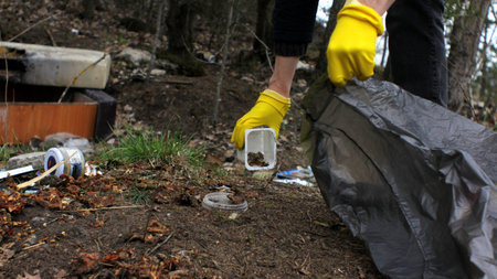 Hand of volunteer picking up garbage in the forest