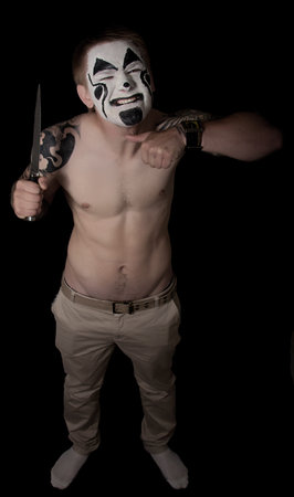 pumped up young man with tattoos and painted face with a knifeの写真素材