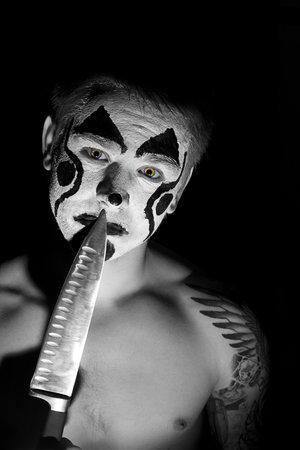 pumped up young man with tattoos and painted face with a knifeの写真素材