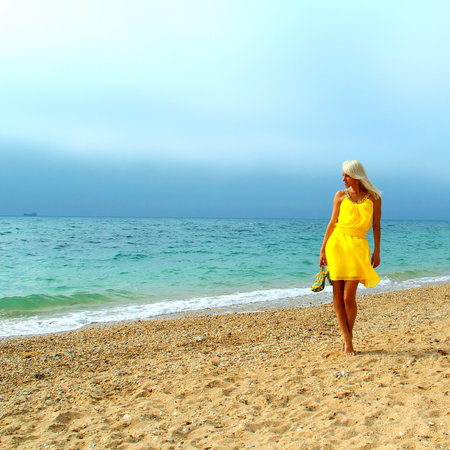 Beautiful tanned blonde girl in a yellow dress on the beachの写真素材