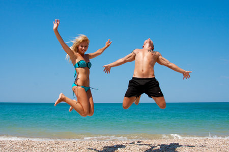 Young happy beautiful couple jumping in the beachの写真素材
