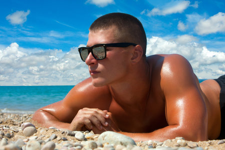 A man with a beautiful muscular body relaxing on the beachの写真素材