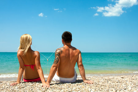 Young happy guy and girl listening to music through headphones on the beachの写真素材