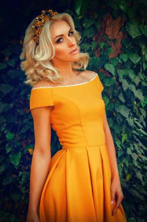 A stunningly beautiful woman wearing a crown and evening 
yellow dress in the woods, on a background of greenの写真素材