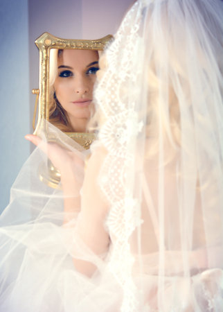 beautiful bride in a veil admiring themselves in the mirror. The reflection in the mirrorの写真素材