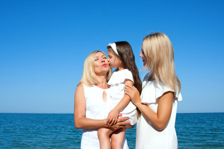 Beautiful Mom with daughter and grandmother relaxing and having fun on the beachの写真素材
