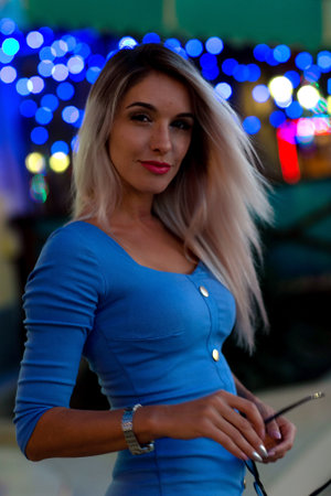 A blond woman with long hair and a beautiful slim figure in a blue dress. Portrait against the lights of the night city.の写真素材