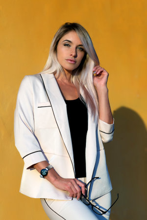 Beautiful blonde in a beige trouser suit and glasses against the background of an orange wallの写真素材