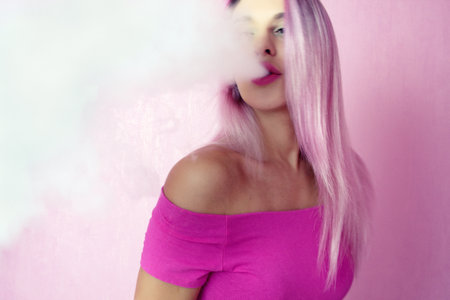 Beautiful sexy woman with pink hair smokes electronic cigarette. On style.の写真素材
