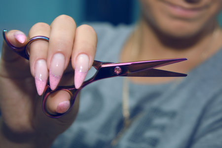Female Hairdresser's Hands with long, well-groomed nails hold beautiful hair clippers.の写真素材