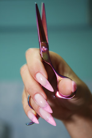 Female Hairdresser's Hands with long, well-groomed nails hold beautiful hair clippers.の写真素材
