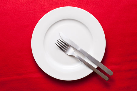 White empty plate with fork and knife on red tableclothの写真素材