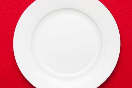 White empty plate with fork and knife on red tablecloth の写真素材