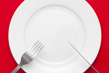 White empty plate with fork and knife on red tablecloth の写真素材