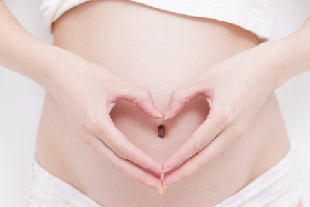 Woman holding her hands in a heart shape on her pregnant belly 