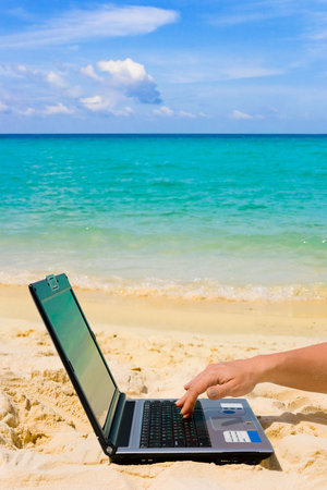 Computer and hand on beach, business travel background の写真素材