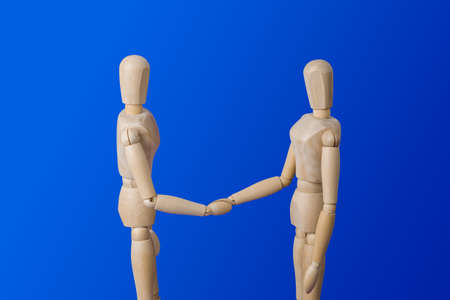 Wooden toy figures handshake on blue background