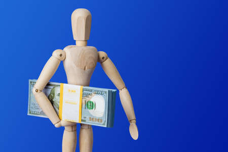Wooden toy figure with money on blue backgroundの写真素材