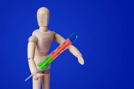 Wooden toy figure with thermometer on blue backgroundの写真素材