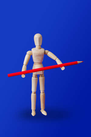 Wooden toy figure with pencil on blue background
