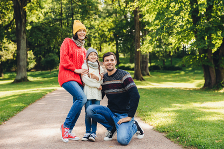 Carefree restful family have walk together, enjoy sunny autumn weather, green beautiful park and fresh air, pose into camera, embrace each other, have model relationship. Joyful child and parentsの写真素材