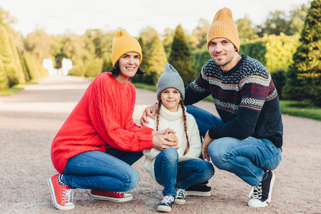 Friendly family wear knitted clothes, have walk together, admire splendid autumn weather. Affectionate young parents and their little cute daughter play together outdoor. Relationship conceptの写真素材