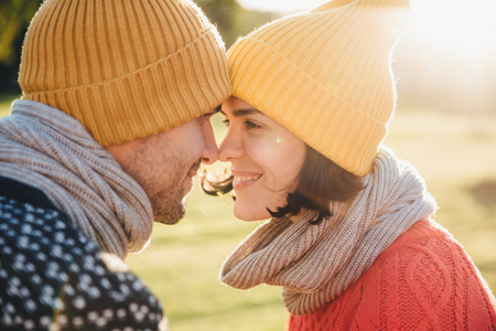 Outdoor portrait of lovely female and her boyfriend, look at each other`s eyes, keep noses together, enjoy calmness and togetherness. Handsome young man and his girlfriend have good time togetherの写真素材