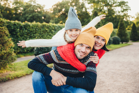 Handsome young man spends his free time with family, recieves embrace from adorable daughter and pretty wife, have picnic during autumn weekend. Happy affectionate family have good relationships.の写真素材