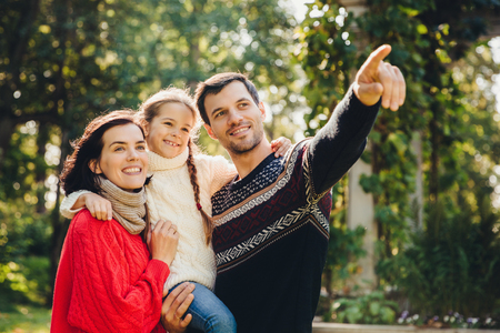 Outdoor portrait of smiling happy friendly family have walk together. Affectionate father shows his small daughter something into distance. Family admire sunrise, beautiful nature, wear warm clothesの写真素材