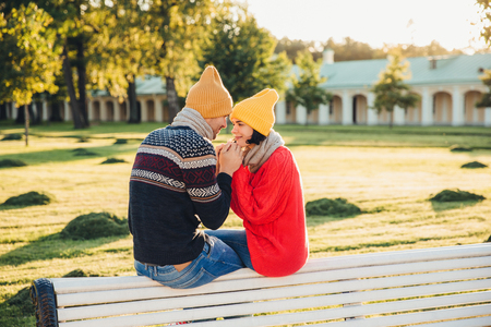 Romantic couple sit on bench, enjoy sunny day, keep hands together, look with great love at each other, have good relationships. Female has date with boyfriend in park, admire beautiful natureの写真素材