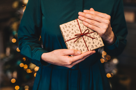 Cropped shot of unrecognizable woman in festive dress being glad to recieve christmas present from husband stand against New Year decorated fir tree. Congratulation and celebration conceptの写真素材
