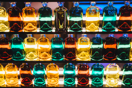 Background with different colored bottles placed on illuminated shelves.の写真素材