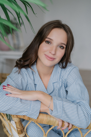 Pleased charming female with dark hair, make up, dressed in elegant costume, poses at home at wicker furniture, poses indoor, has spare time. People, beauty, free time and lifestyle concept.の写真素材