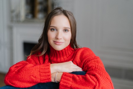 Shot of pleasant looking young brunette girl has good rest at home, looks directly at camera, has healthy skin, spends free time in domestic atmosphere alone. People, beauty, free time conceptの写真素材
