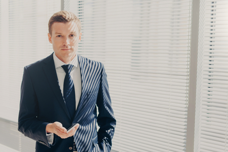 Confident male entrepreneur in formal suit, chats in social networks, recieves discount for mobile internet, has serious expression, thinks about startup, being professional worker. Technology conceptの写真素材
