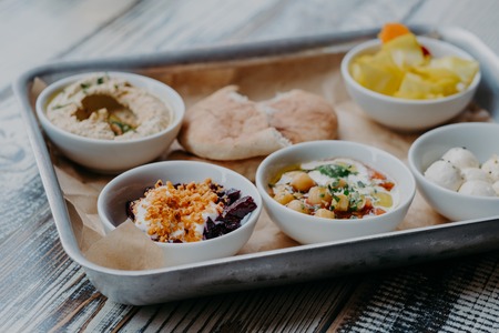 Food and nutrition concept. Traditional Israel dish for dinner. Tray of delicious hummus, beet with spices, core of tomatoes, pita bread, goat cheese served for youの写真素材