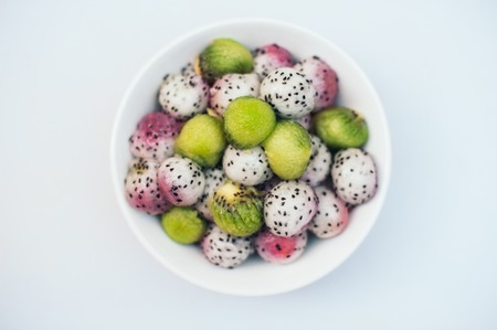Tasty fruit dessert. Dragon fruit and kiwi balls in bowl isolated over white background. Exotic fruit salad. Carving concept. Ripe pitahaya in form of ballsの写真素材