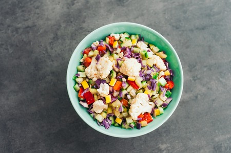Top view of fresh vegetable salad with cauliflower, purple cabbage, chopped red bell pepper and cucumber. Delicious meal in bowl. Eating and nutrition conceptの写真素材