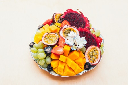 Red pitaya dragon fruit, grapes, mango and strawberry on plate against white background. Good nutrition, fruit rich in vitamins. Fresh salad. Tropical fruitsの写真素材