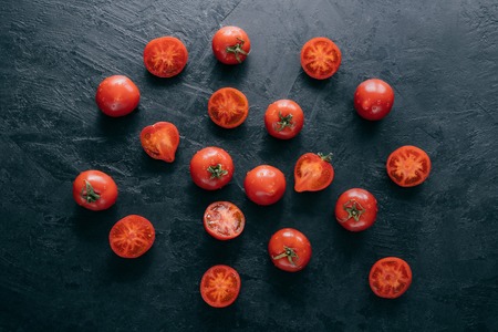 Fresh spring vegetables on dark background. Cherry ripe red tomatoes with green leaves, half sliced tomato, water drops. Organic foodの写真素材