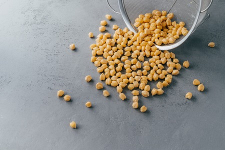 Boiled chickpeas spill out from sieve. Garbanzo grains. Eco product. Dry peas. Copy space. Nut...