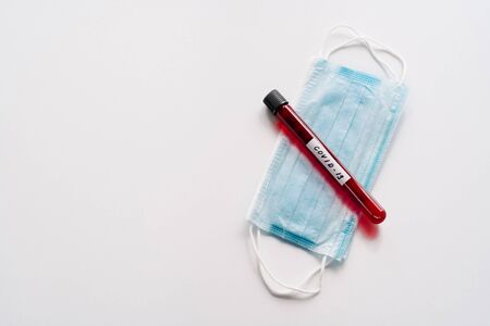 Test tube containing blood samples for coronavirus testing or analyzing, sterile medical mask on...