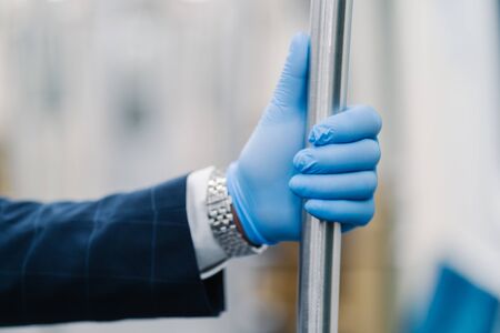 Mans hand in blue disposable glove touching handrail in public transport. Pandemic precaution. Protection against viruses and bacteria. Coronavirus and viral disease protection. Male passengerの写真素材