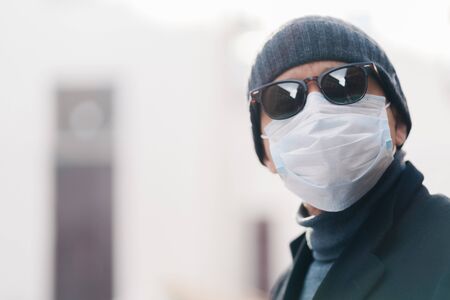 Close up shot of man wears hat and disposable medical mask, afraids of getting infected with...
