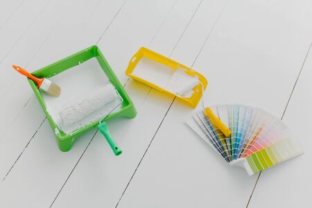 Top view of paint trays, brushes and rollers, color palette sample, white floor. Tools for making...